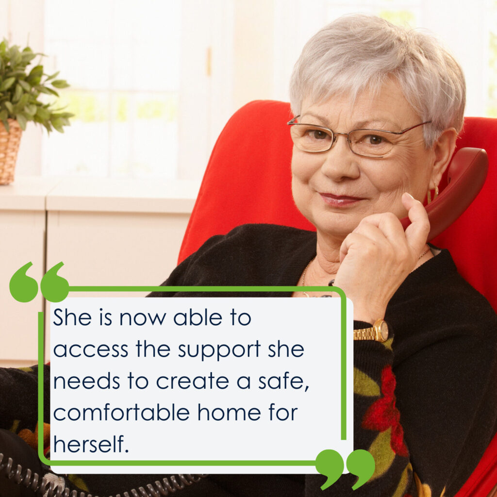 A lady with grey hair holding a red phone and sitting in a red chair. She is looking at the camera and smiling. The quote on the picture says 'She is now able to access the support she needs to create a safe, comfortable home for herself.'