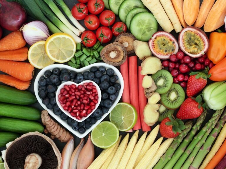 a heart shaped bowl filled with fruits and vegetables all scattered around it.