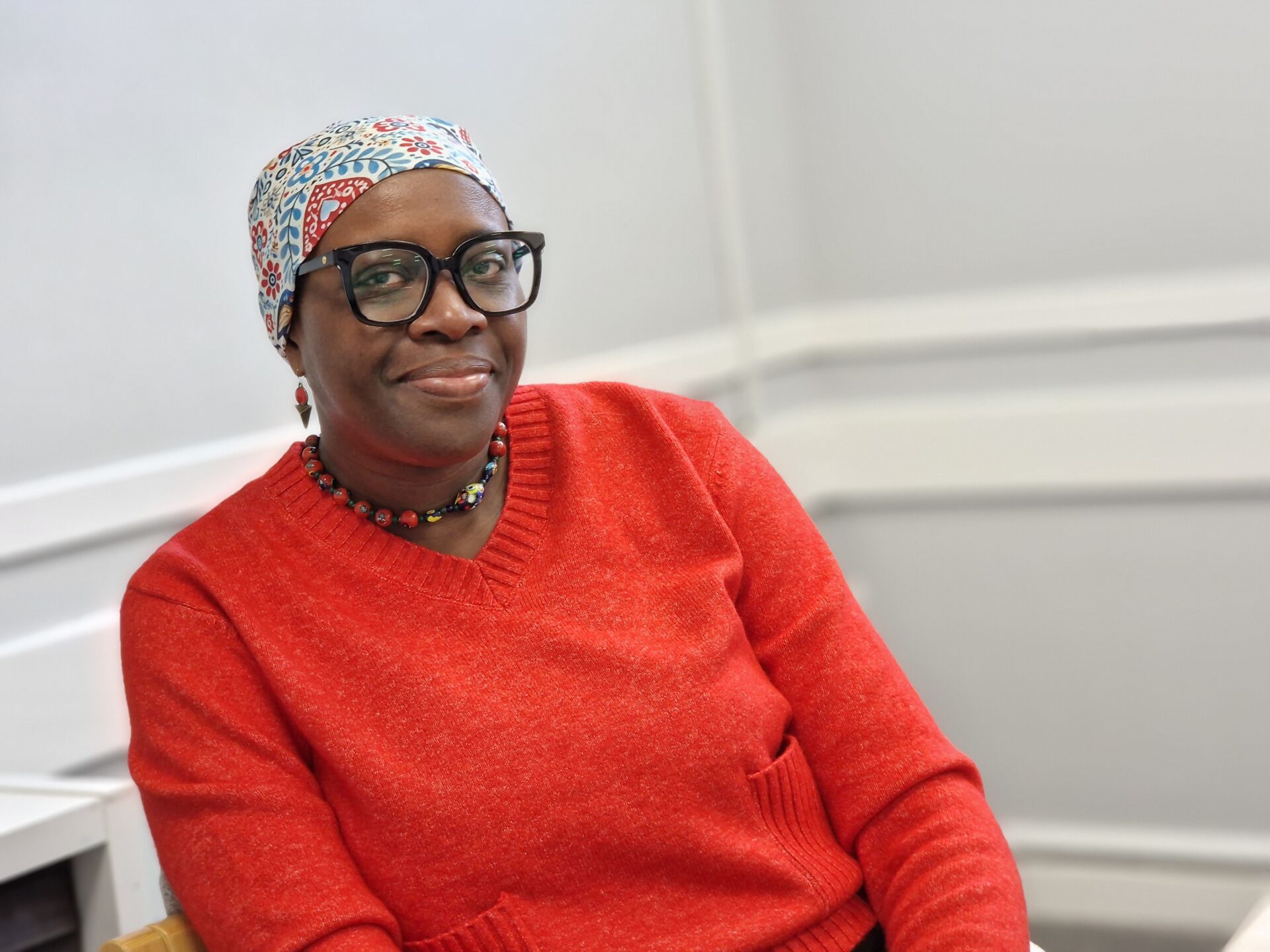“Finding strength through support: Dolly's cancer journey” 3 A lady wearing a headscarf and glasses is looking directly at the camera. She is wearing bright clothing.