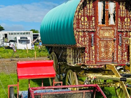 A gypsy bow top caravan and a trap for a pony are sat in a field at the Appleby horse fair i