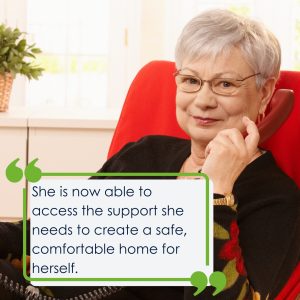 A lady with grey hair holding a red phone and sitting in a red chair. She is looking at the camera and smiling. The quote on the picture says 'She is now able to access the support she needs to create a safe, comfortable home for herself.'