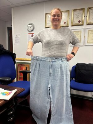 Tracy holding up her old pair of jeans showing her weight loss.